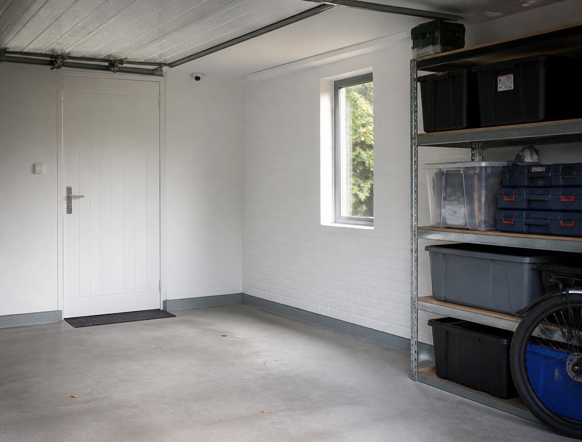 Clean white-painted garage in Eastney with shelving, a side door and a CCTV camera